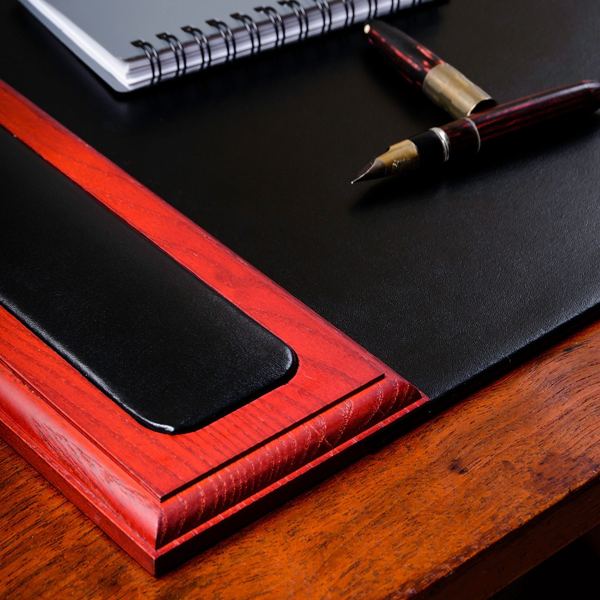 Red leather-bound book with black leather mat on a wooden surface, next to a fountain pen.